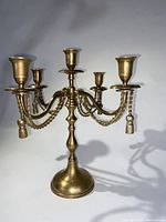 Front view of vintage solid brass 4 arm candle candelabra with braided rope and tassel trim, showing detailed arm and tassel design.
