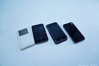 Front view of 4 devices: white iPod, two black iPhones, one with cracked screen