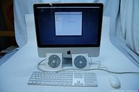 Apple iMac 20-inch all-in-one desktop with screen turned on showing setup screen. Includes keyboard, mouse, and two OS CDs in sleeves placed in front.