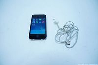 Front view of black Apple iPhone 4 showing screen on with icons. Includes white USB charging cable coiled next to phone.