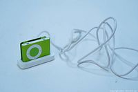 Apple iPod Shuffle 2nd Generation green color inserted in white charging dock with USB cable attached.