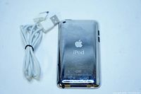 Back side of Apple iPod Touch shows Apple logo, product details, scratches on metal casing, and included charging cable.