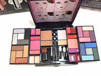 Top view of open makeup palette showing a wide spectrum of eyeshadow colors, lip glosses, and highlighters arranged neatly with application tools.