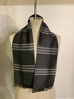 Front view of scarf displayed on mannequin showing plaid tartan pattern and fringes.