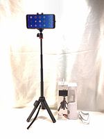 Mobile tripod extended with smartphone mounted horizontally, box packaging and remote beside it.