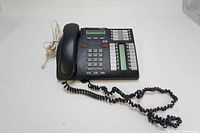 Front view of the black Nortel Avaya T7316e phone showing the handset, numeric keypad, programmable memory keys, and LCD screen.