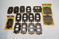 Full set of vintage Amerock Carriage House electrical outlet and switch covers laid out on white surface with some still in original packaging.