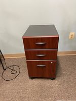 Front view of the Bush Business Furniture 3 drawer mobile pedestal showing wood grain finish, dark handles on the drawers, and caster wheels at the base.