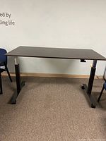 Side view of the adjustable height desk showing metal legs and rectangular black top.