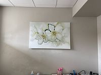 Rectangular canvas painting of white flowers hanging on a beige wall above a desk area.