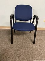 Front view of a single blue cloth office chair showing seat, backrest, and black metal armrests and legs