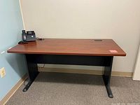 Front view of Bush Business Furniture office desk with wood finish top and black metal legs, showing cable management grommet and clean surface.