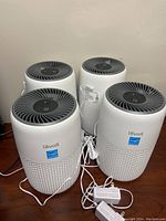 Four white Levoit Core Mini air purifiers with grey top fan grills and accompanying power adapters