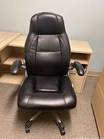 Front view of black faux leather office chair positioned in front of a wooden desk unit.