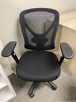 Front view of black office chair with mesh back and padded seat, adjustable armrests.