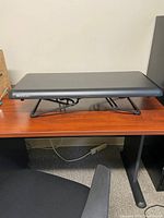 Side view of black rectangular Varidesk platform showing smooth surface and metal legs
