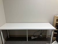 Front view of white rectangular IKEA desk with six cylindrical white legs, placed against a wall.