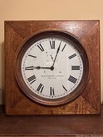 Front view of the antique clock showing square quarter sawn oak case and round clock face with Roman numerals and black hands.