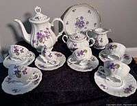 Full set arranged on dark cloth showing teapot, six cups and saucers, sugar bowl, cream pitcher, and dessert plate with pansy design