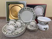 Photo showing the complete set of five plates, four cups, four saucers, two serving bowls closed with holly berry design and gold trim, plus four new boxed gold metallic chargers.