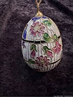 Front view of the decorated cloisonné egg ornament showing floral patterns and hanging loop