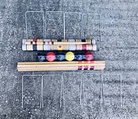 Wooden mallets, croquet balls, and metal hoops laid out on concrete surface