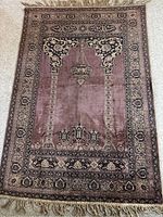 Full view of a fringed area rug with prayer arch design and floral borders on carpeted floor.