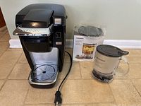 Keurig coffee maker and Teavana Perfectea Maker with box on tile floor, showing both items clearly.