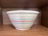 Side view of a large vintage McCoy ovenware mixing bowl with off-white glaze and pink and blue stripes around the exterior.