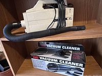 Oreck XL vacuum cleaner on shelf with hose attached and 12 Volt Jumbo Auto vacuum cleaner in box beside it