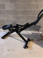 Side view of Power Rider exercise machine showing black metal frame, padded seat, and hydraulic resistance mechanism.