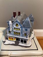 Front and angled view of the hand-painted Antique Shop sculpture showing detailed architecture and coloring on a snow-covered base.