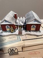 Close-up angled view from above of the red brick sculpture with roof details, windows, and the snowy base. The sculpture depicts a winter setting and intricate architectural details.