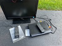 Photo of Toshiba 19-inch TV and Sony Blu-ray player with both remote controls and connecting cables visible, devices placed outdoors on asphalt.