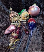Vintage glass Christmas ornaments laid on black fabric showing seven varied ornaments: pinecone, teardrop, finial, round ball, spiral-shaped, small house, and greetings ornament.