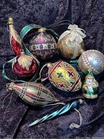 Full view of all eight vintage glass Christmas ornaments on a black cloth background showing variety in shapes, colors, and patterns.