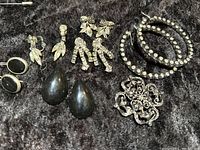 Photo showing vintage earrings, bracelets, and brooches arranged on dark fabric with visible rhinestones and black accents.