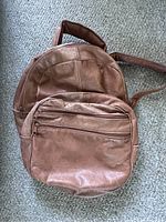 Front view of the vintage brown leather backpack showing front zippered pockets and overall condition.