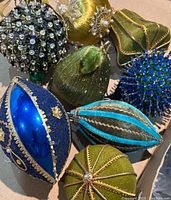 Photo showing cluster of nine vintage Christmas ornaments in olive green, gold, and various shades of blue featuring felt, fabric, bead, and metal embellishments.