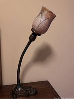 Full view of the lamp showing the gooseneck arm, iridescent glass shade, and metal base with decorative design.