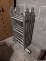 Folded Werner aluminum multi-position ladder stored in a corner on concrete floor.