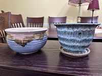 Image showing a pair of pottery planters: a taller blue speckled one with attached saucer and a shorter blue and brown glazed one, displaying their overall shape and glaze.