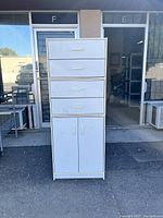 Front view of a white stacking cabinet with four drawers on top and a two-door cabinet below, placed outdoors in front of a building door