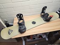 Full view of the snowboard showing the bindings mounted on top and the graphics visible on the deck.