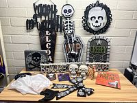 Full lot of Halloween decorations including wooden signs, skull and skeleton props, ghost costume, buntings, and treat bags arranged on a table and hung on the wall.
