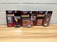 Five Starting Lineup Timeless Legends sports action figures in original packaging, sitting side by side on wooden surface against white brick wall.