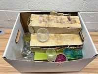 Box containing multiple glass candle holders of various colors and styles