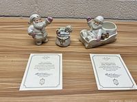 Lot showing all three Lenox Santa-themed figurines with three certificates of authenticity on wooden surface.