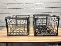 Two vintage metal milk crates side by side, showing the rectangular shape, wire mesh sides, and different base patterns.