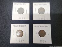 Four Indian Head Cents in white cardboard coin holders with years 1899, 1900, 1902, and 1904 visible.